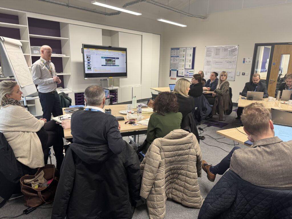 A speaker addressing a group of colleagues in a classroom attending a training session